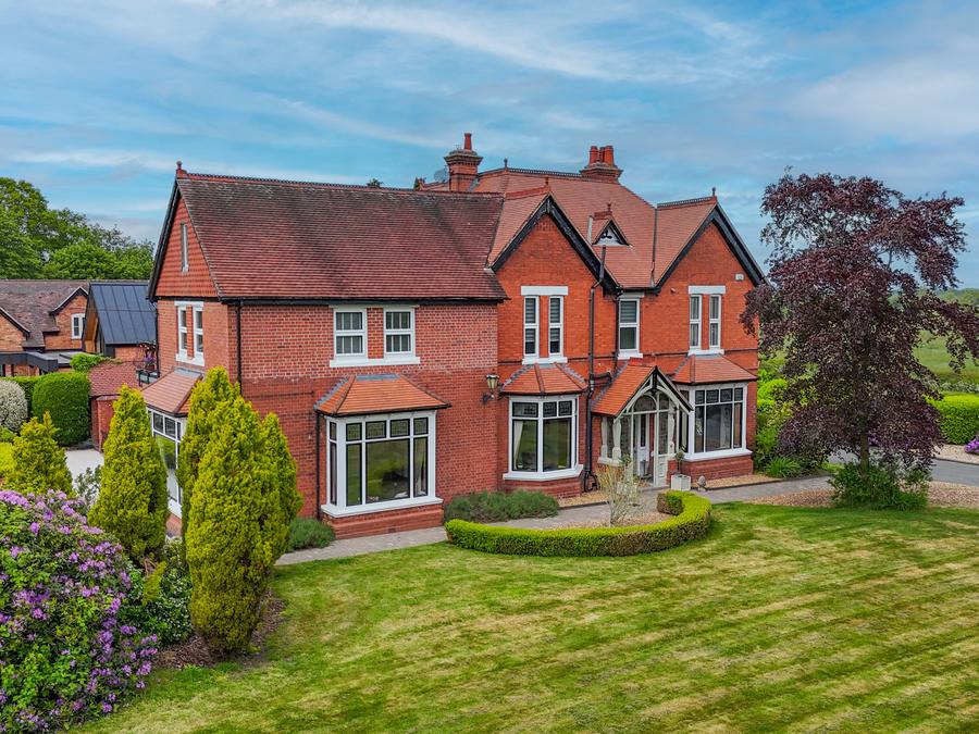 Red-brick Victorian house with bay windows, seen from the air above its lawned garden
