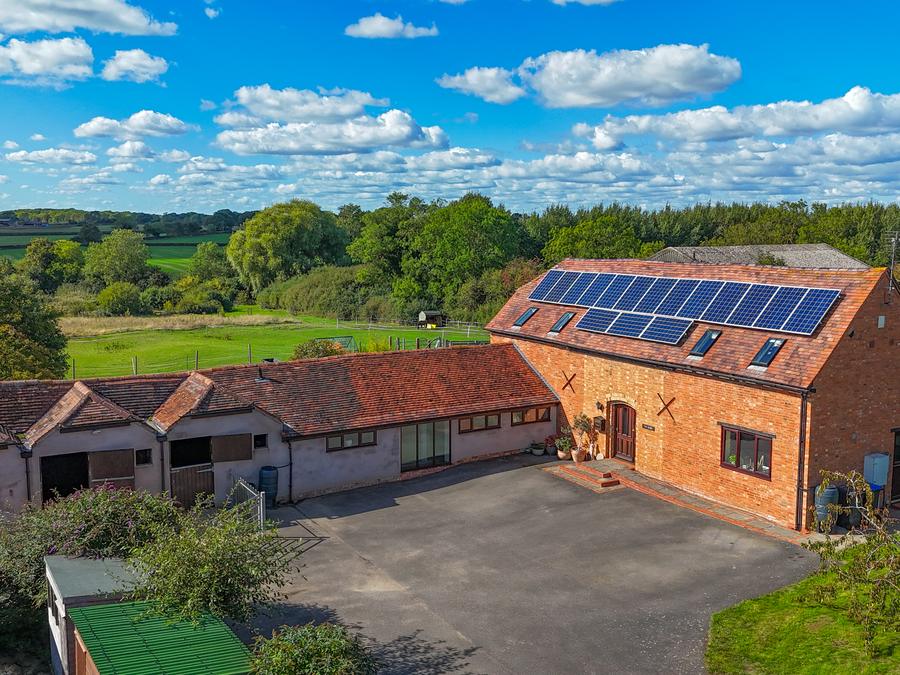 Brick barn conversion with roof-mounted solar panels, farmland behind
