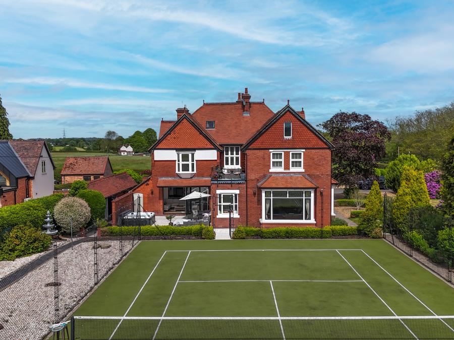 Red-brick house above a grass tennis court, with terraced gardens and mature trees