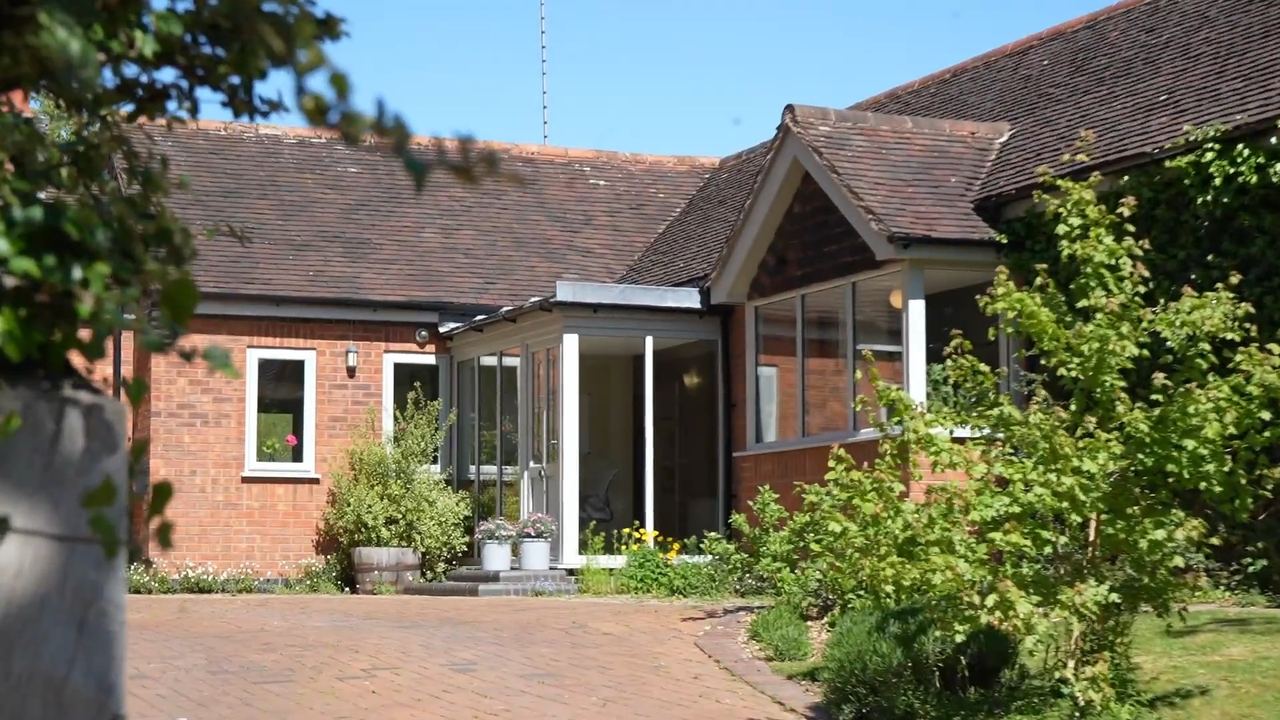 The Stables: a long brick house with a conservatory, seen across the garden