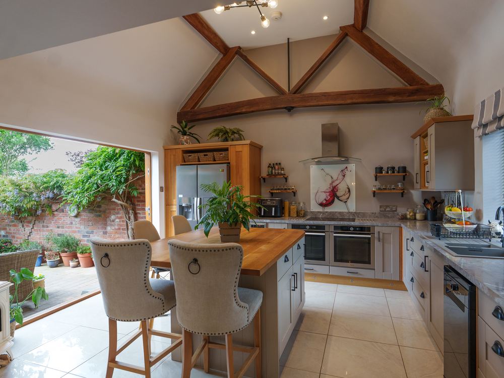 Kitchen under a vaulted ceiling with exposed trusses, bi-fold doors open to a courtyard