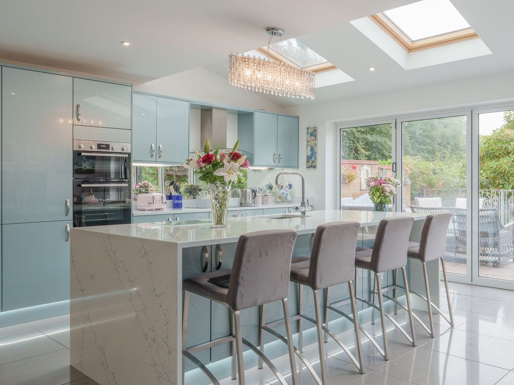 Pale blue gloss kitchen with a marble-topped island and bar stools beneath roof lanterns