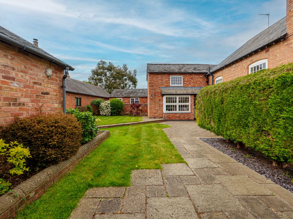 Red brick house seen across a lawn, with a clipped hedge along a paved path