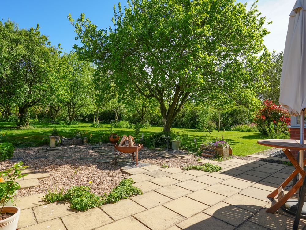 Garden with mature trees, a paved terrace and a folded parasol