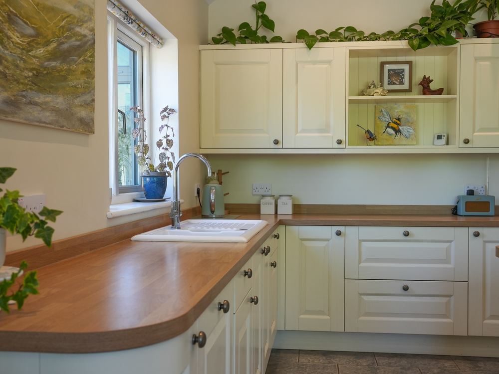 Cream shaker kitchen with a curved timber worktop and a sink beneath the window