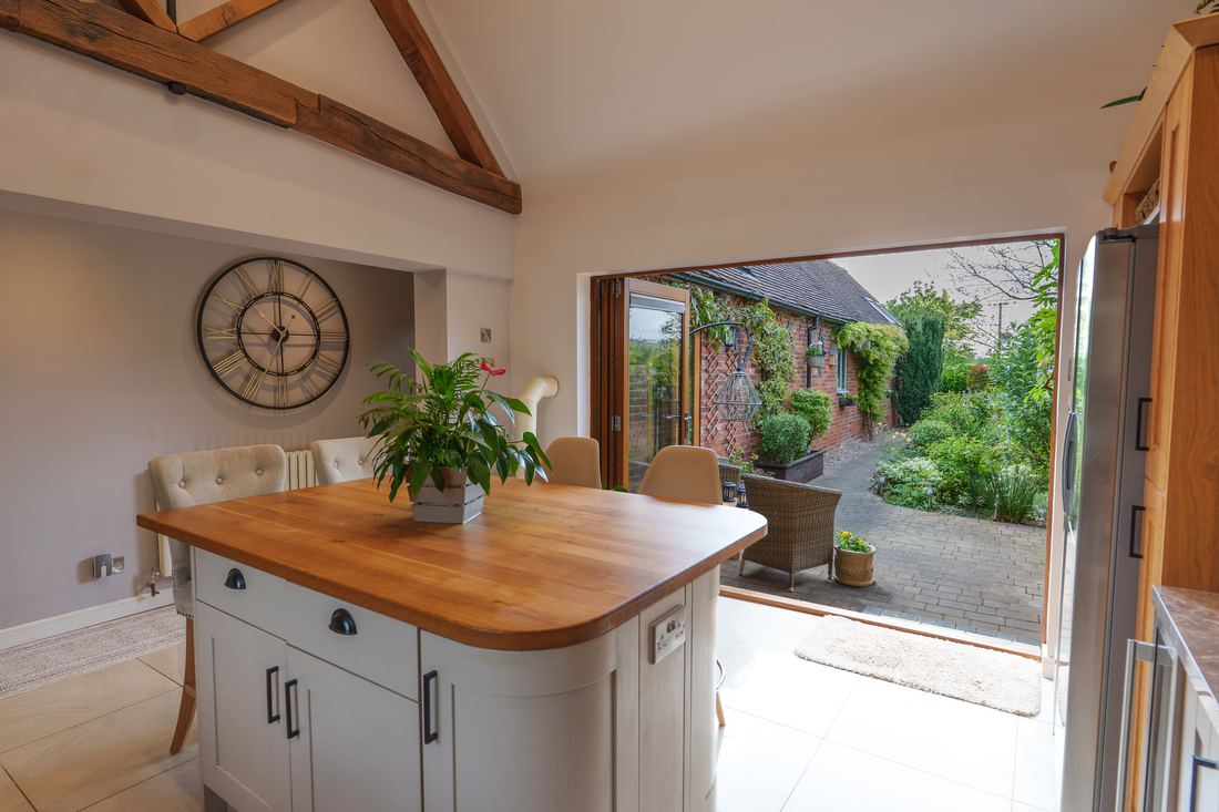 Kitchen island with an oak worktop, doors folded back to a walled courtyard