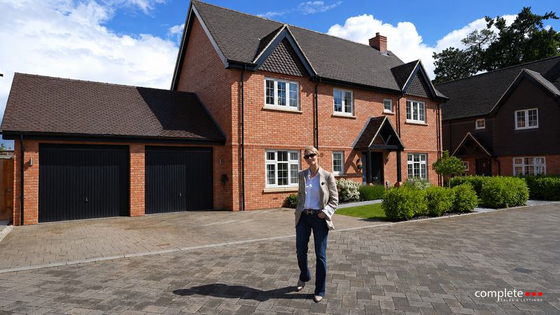 An agent walking across the driveway of a new red-brick house with a double garage