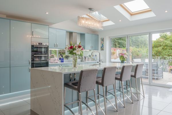 Pale blue gloss kitchen with a marble island beneath roof lanterns