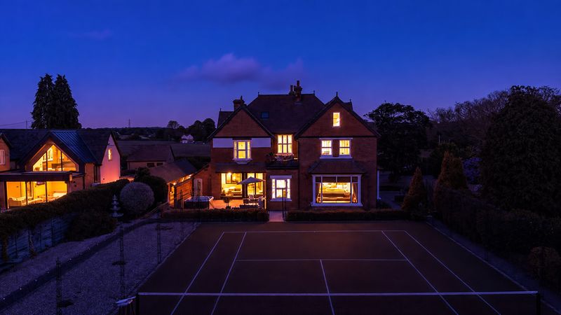 A house and its tennis court at blue hour, every window lit warm