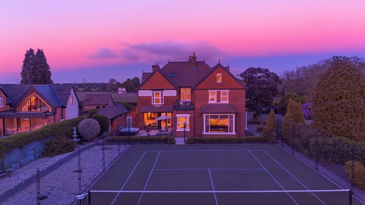An aerial view of a house and tennis court under a deep pink sunset.